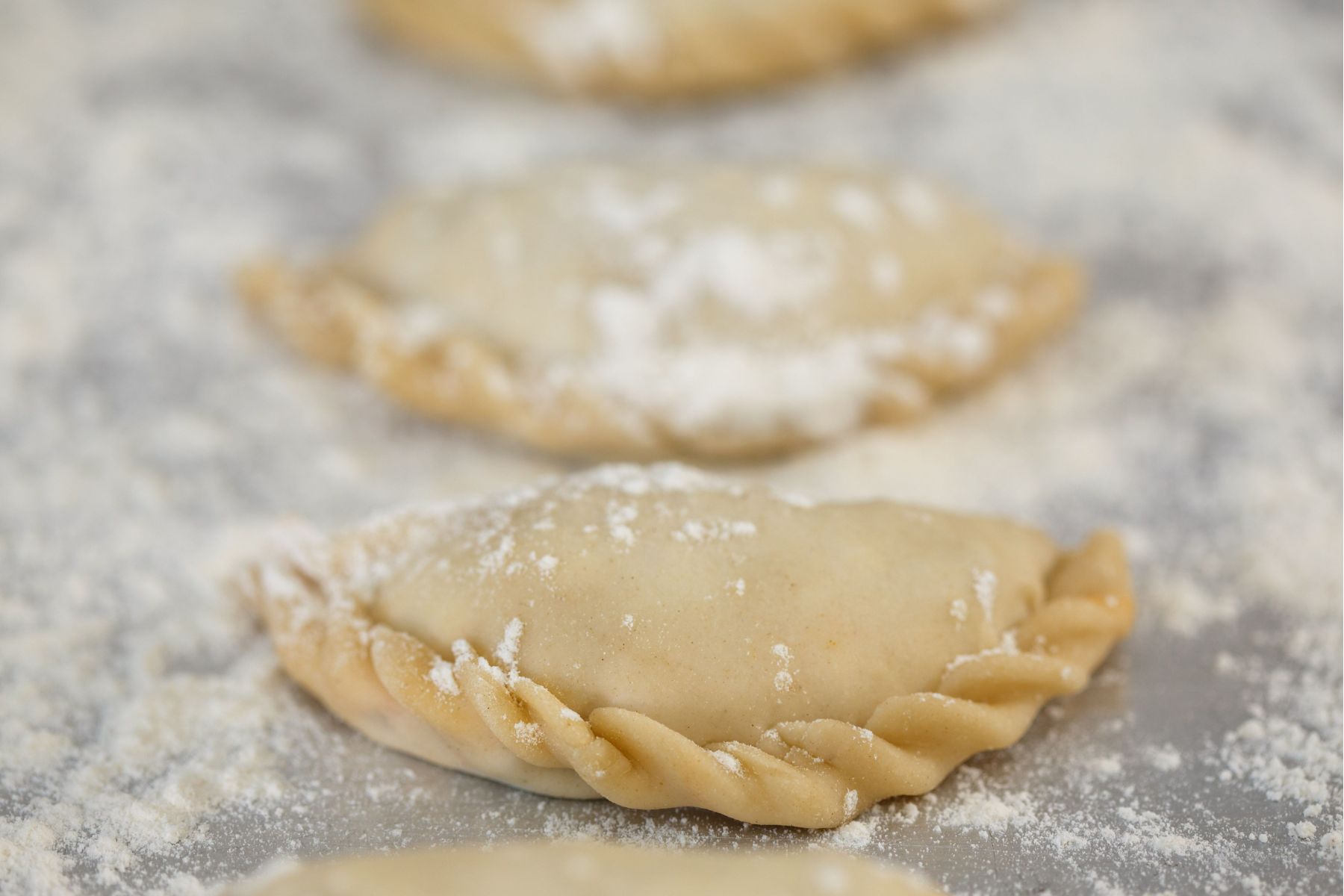 Close-up of uncooked dumplings with crimped edges, dusted with flour, resting on a floured surface.