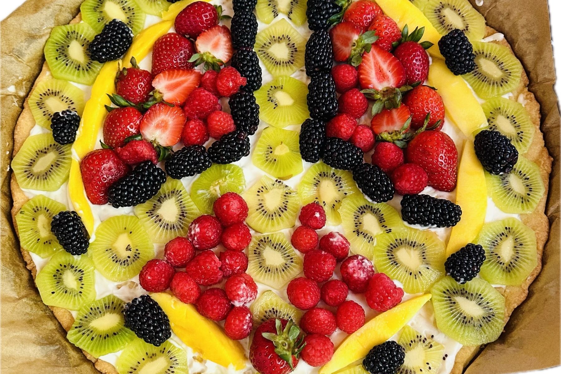A fruit tart topped with sliced kiwi, strawberries, blackberries, raspberries, and mango, arranged in a colorful pattern on a creamy base and a golden crust.