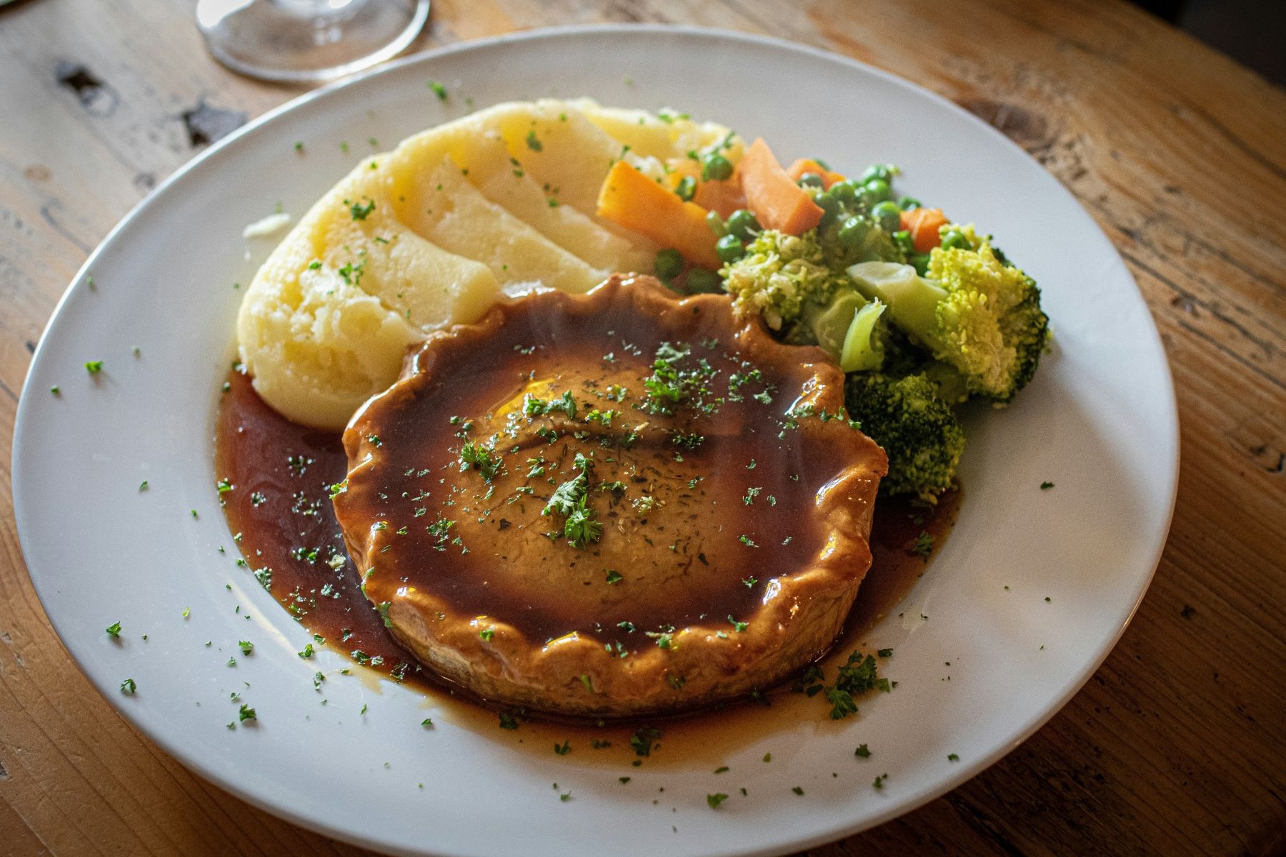 A savory pie covered in gravy, served with a scoop of mashed potatoes and a side of mixed vegetables.